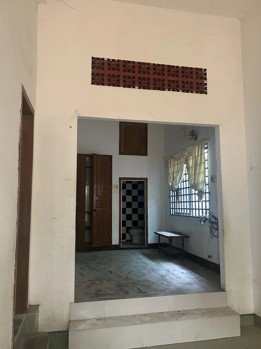 Inside before renovation: a red concrete vent screen above a doorway, steps down into a room with a checkered-tile bathroom and barred window