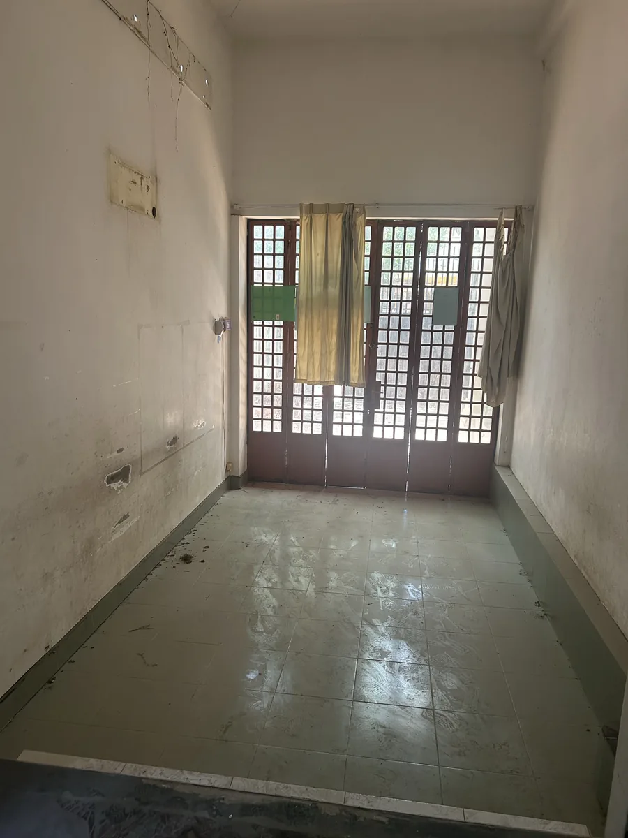 An empty room before renovation with worn walls, old curtains, and original French folding doors letting in the light