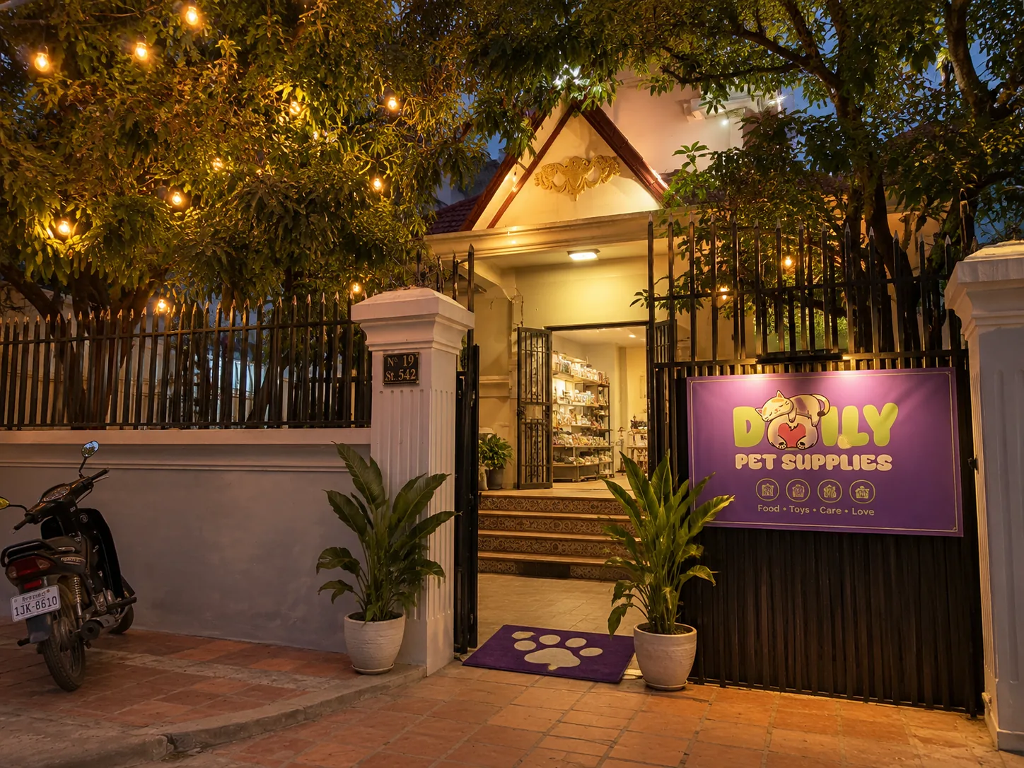 The villa gate at dusk, string lights glowing in the trees, the shop lit warm through the open doors